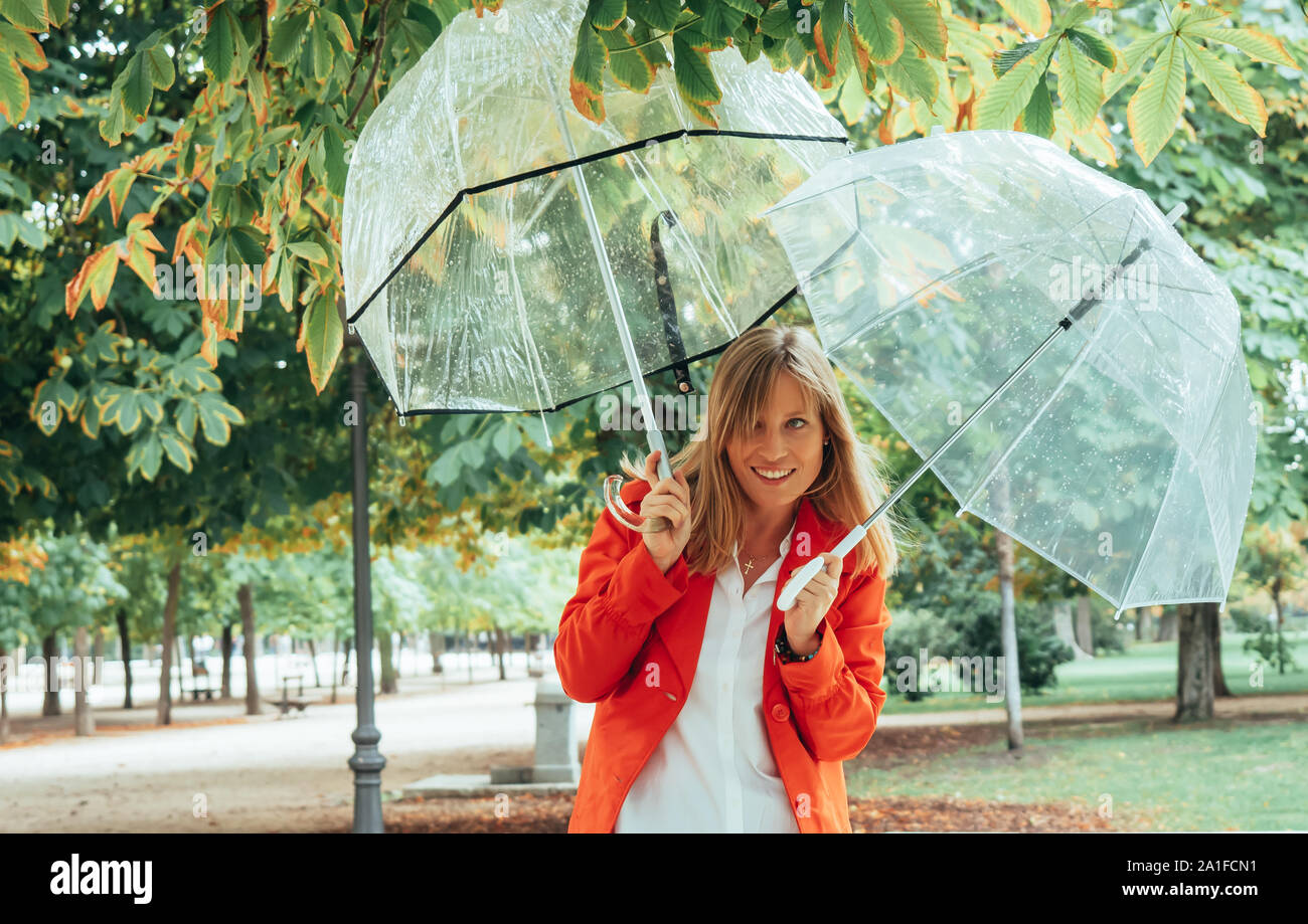 Chica rubia con ojos azules y vestidas de rojo gabardine saldos con dos paraguas  transparente en un parque de Madrid, España Fotografía de stock - Alamy