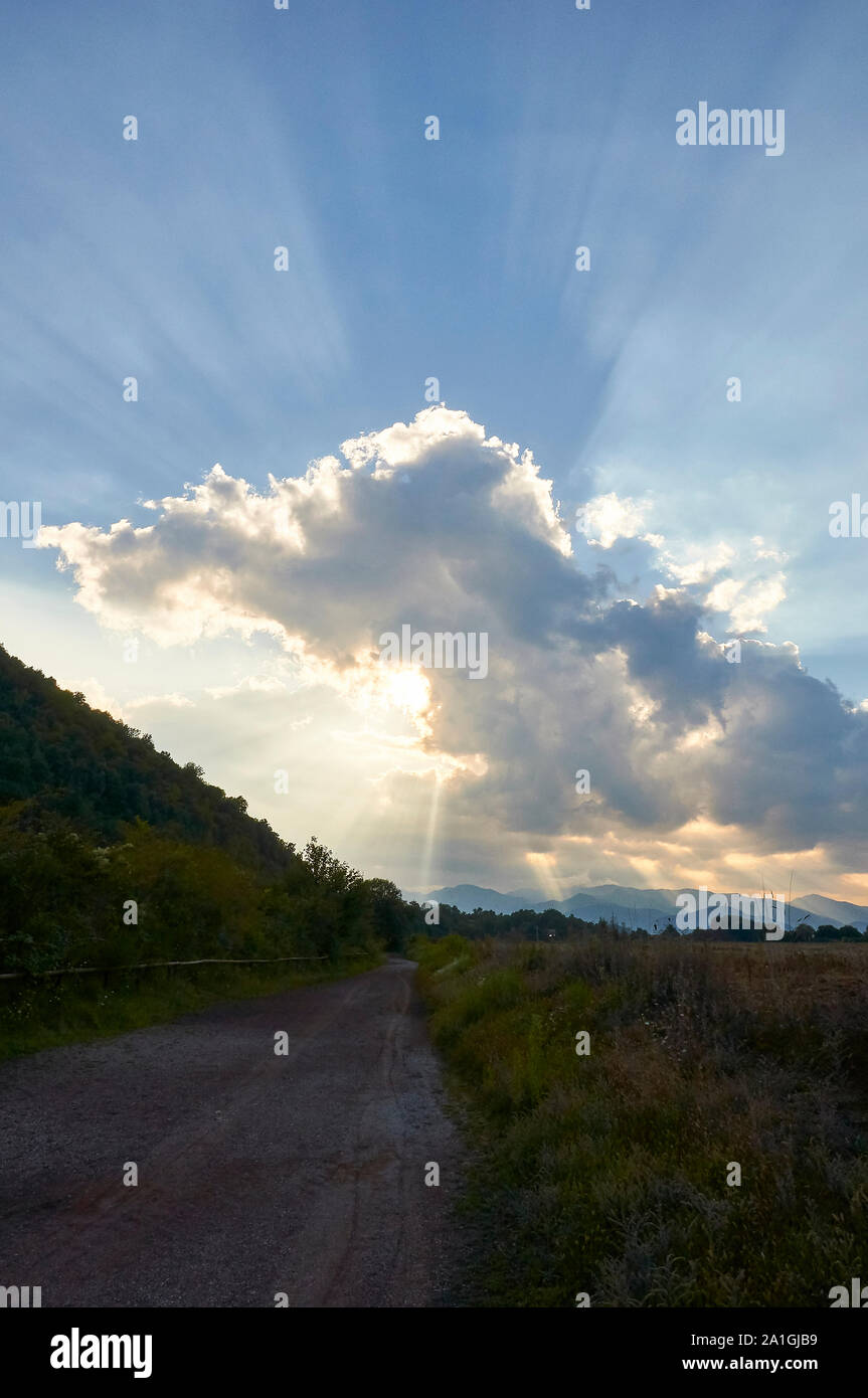 Atardecer con nubes y rayos de sol en sendero por el volcán Croscat en el Parque Natural de la Zona Volcánica de La Garrotxa (Santa Pau, la Garrocha, Girona, España) Foto de stock