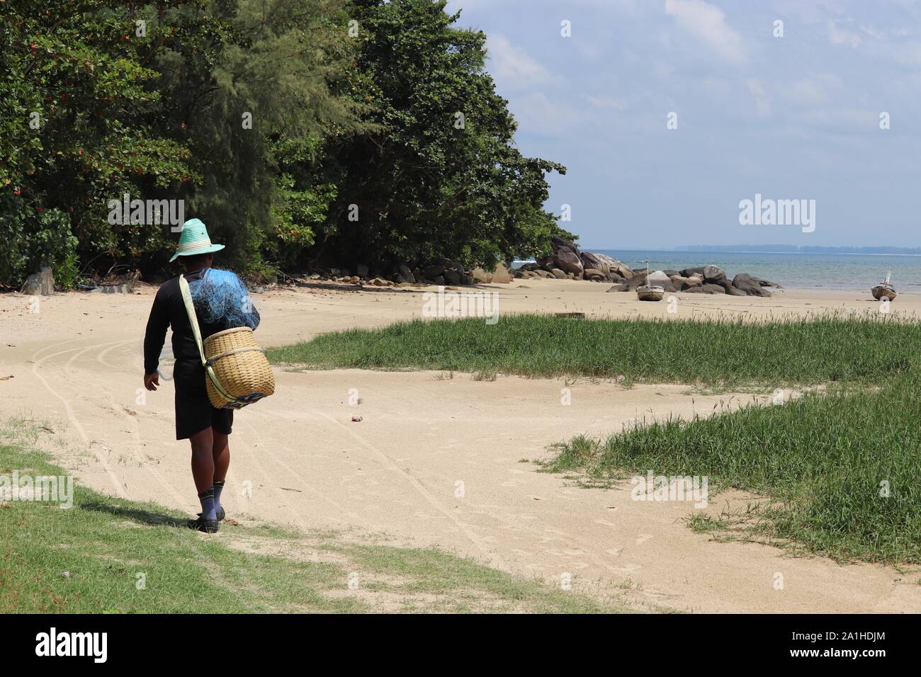 Pescador con una cesta de mimbre y red de pesca va a un mar. El pintoresco paisaje de la costa de Tailandia Foto de stock