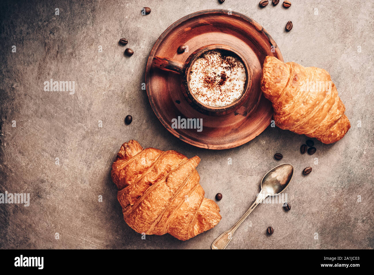 Los cruasanes y café caliente en una taza vintage oscuro sobre un fondo de textura rústica en tonos marrones. Vista desde arriba, laicos plana Foto de stock