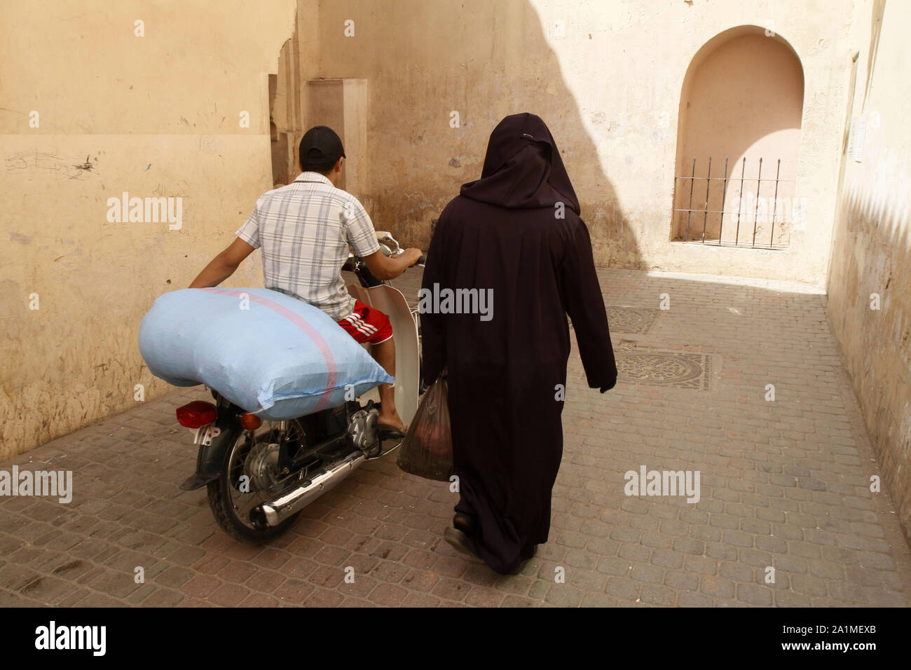 Femme marocaine au Côté d'un homme sur une mobylette transportant une lourde de carga. Marrakech. Maroc. Foto de stock