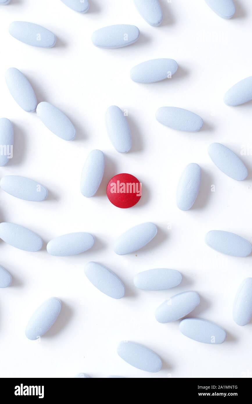 Concepto de placebo. Sola pastilla roja muestra de manera destacada entre las píldoras azul claro sobre fondo blanco. Foto de stock
