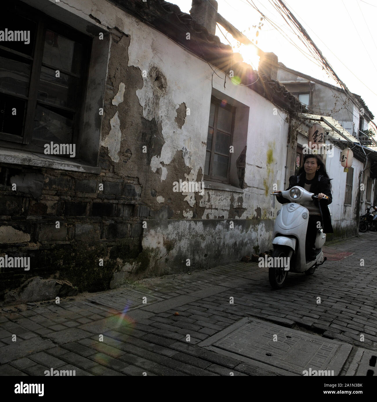 Una mujer está montando con un scooter a través de una calle en la vieja ciudad de Suzhou, China Foto de stock