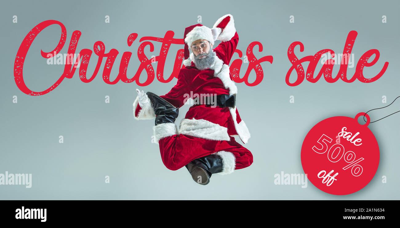 Feliz Navidad Santa Claus en gris de fondo de estudio. Modelo masculino  caucásico en el traje de vacaciones tradicionales. Concepto de vacaciones,  año nuevo, humor, regalos de invierno. Venta de Navidad. Copyspace