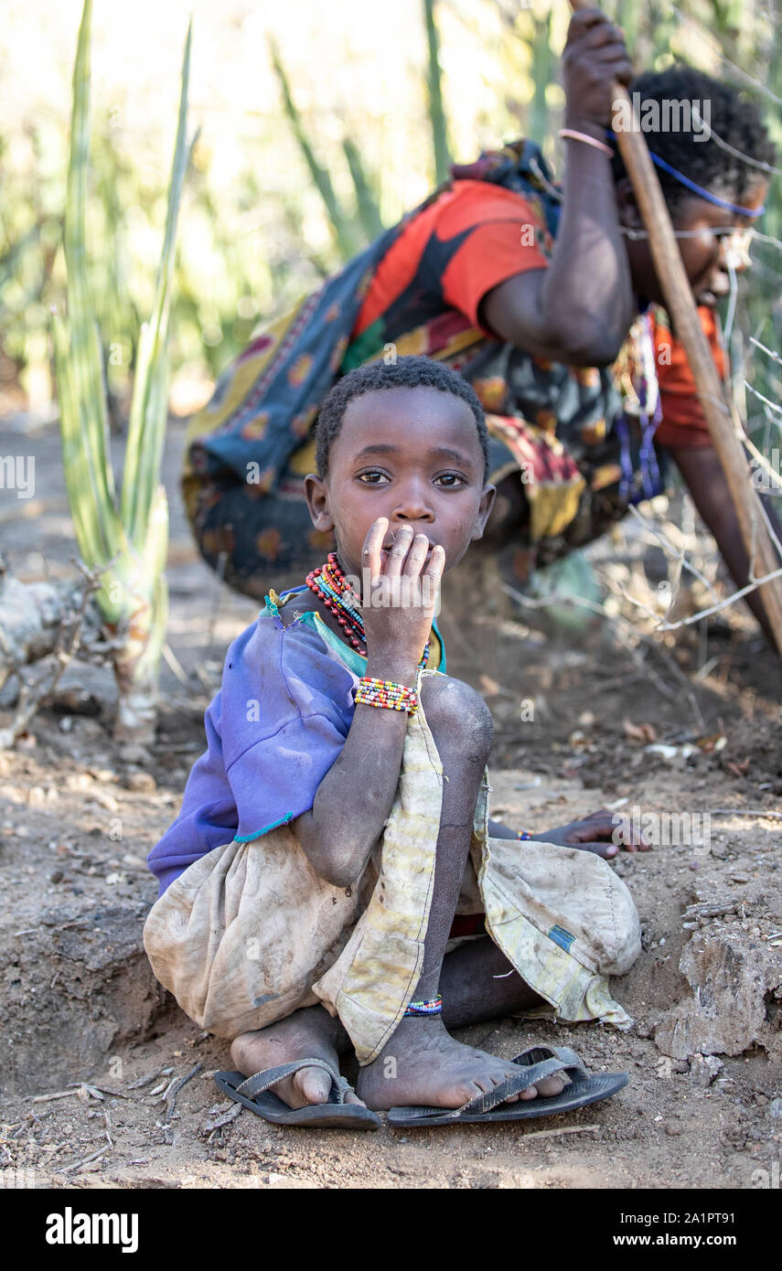 El lago Eyasi, Tanzania, 11 de septiembre de 2019: hadzabe kid con su madre mientras ella está cavando tubérculos para cenar Foto de stock