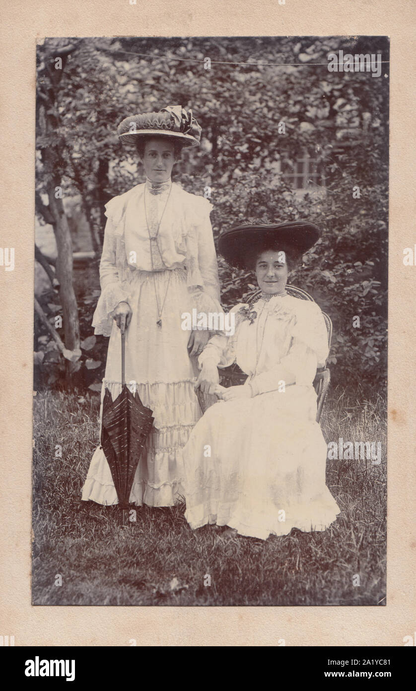 Tarjeta de armario victoriano mostrando dos señoras de moda posando en un jardín. Ambos vistiendo hermosos sombreros. La señora permanente sosteniendo un paraguas. Foto de stock