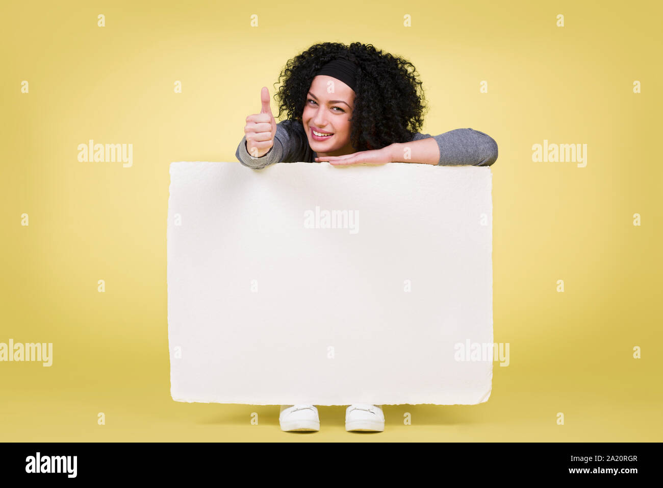 Mujer sonriente sosteniendo un letrero blanco Pizarra con pulgares hacia arriba Foto de stock