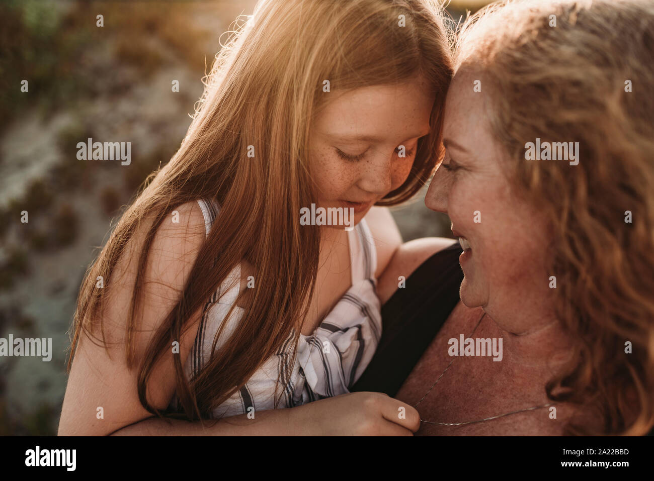 Vista lateral de la madre y la hija de edad primaria pelirroja al atardecer Foto de stock