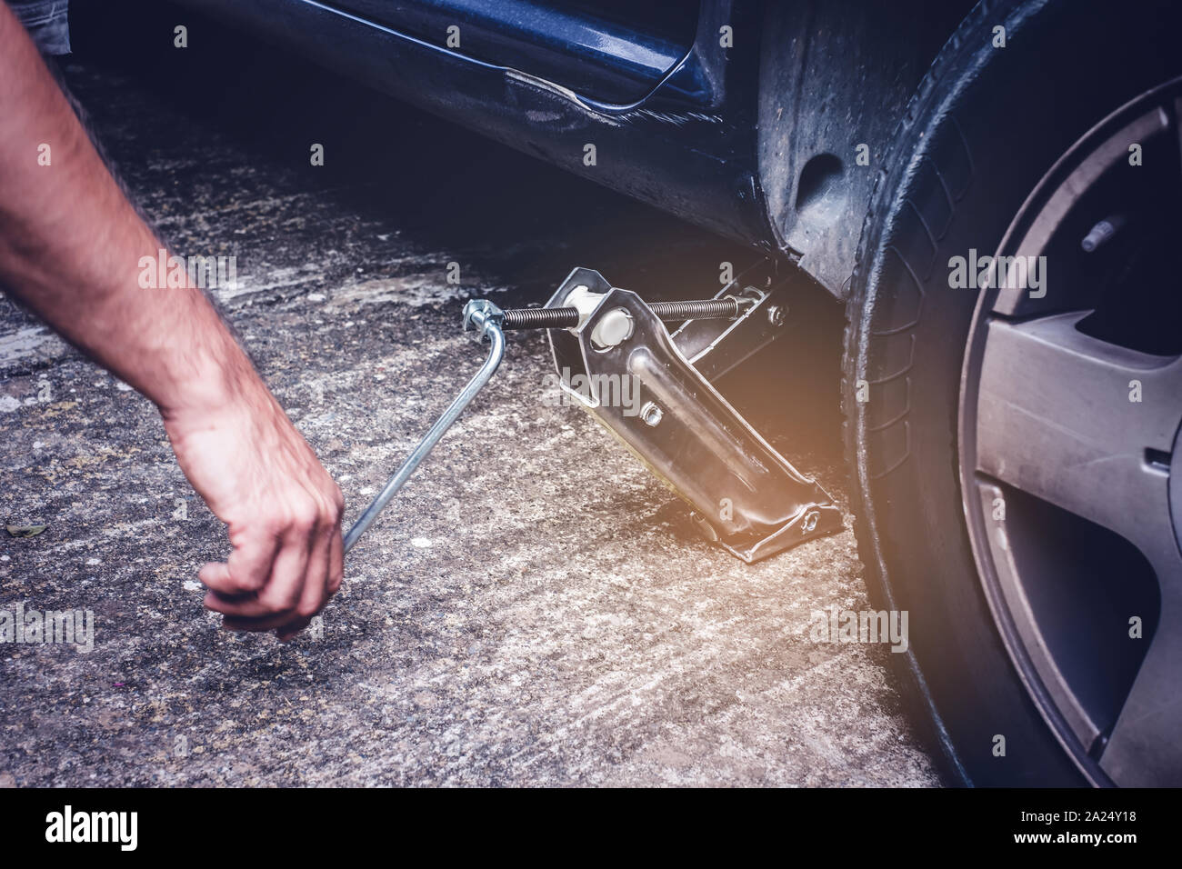El hombre levantando coches con tornillo jack para cambiar los neumáticos de la rueda pinchada - cambio de neumáticos oncept Foto de stock