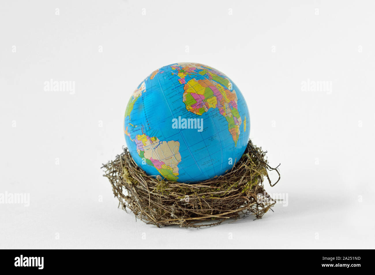 Planeta Tierra en un nido de pájaro sobre fondo blanco - Concepto de conservación ambiental y protección del planeta Foto de stock