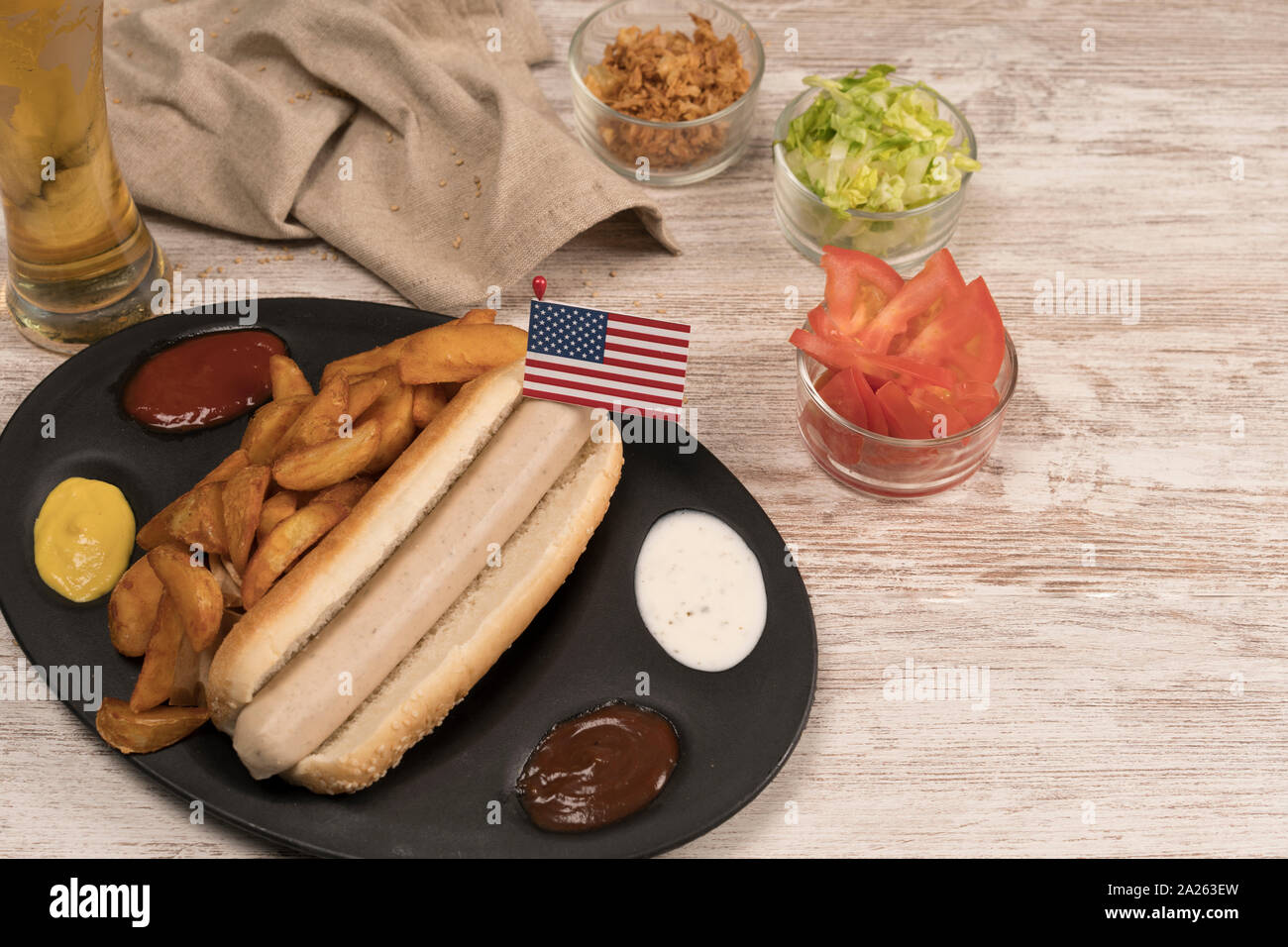 Perro caliente casero con salchichas blancas en bandeja con diversos condimentos y la bandera americana visto desde arriba Foto de stock