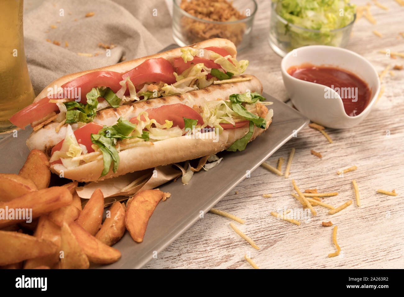 Hot Dog en placa de madera blanca con diversos condimentos en plano medio Foto de stock