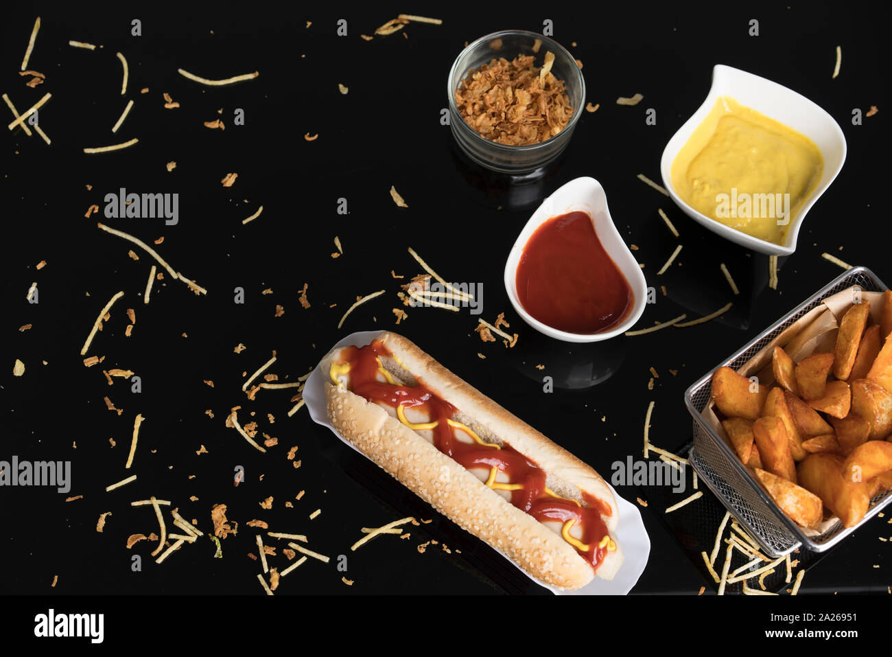 Hot Dog con condimentos, salsas y cuñas de papas.En metacrilato negro Foto de stock