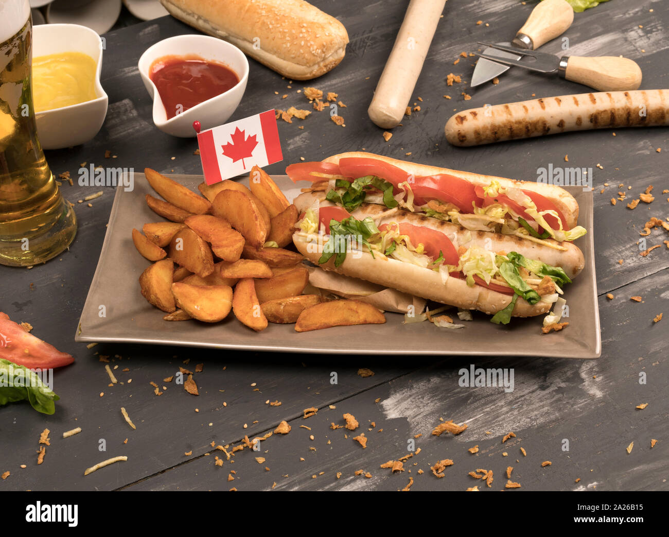 Perro caliente casero con salchichas blancas con diversos condimentos vista delantera del tablero de madera gris y Canadá bandera Foto de stock
