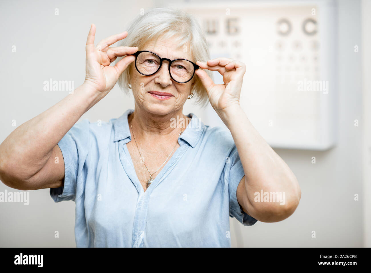 Retrato de una mujer de más edad feliz el uso de anteojos en la parte delantera de la tabla optométrica en oftalmología office. Concepto de control de vista y seleccionar gafas Foto de stock