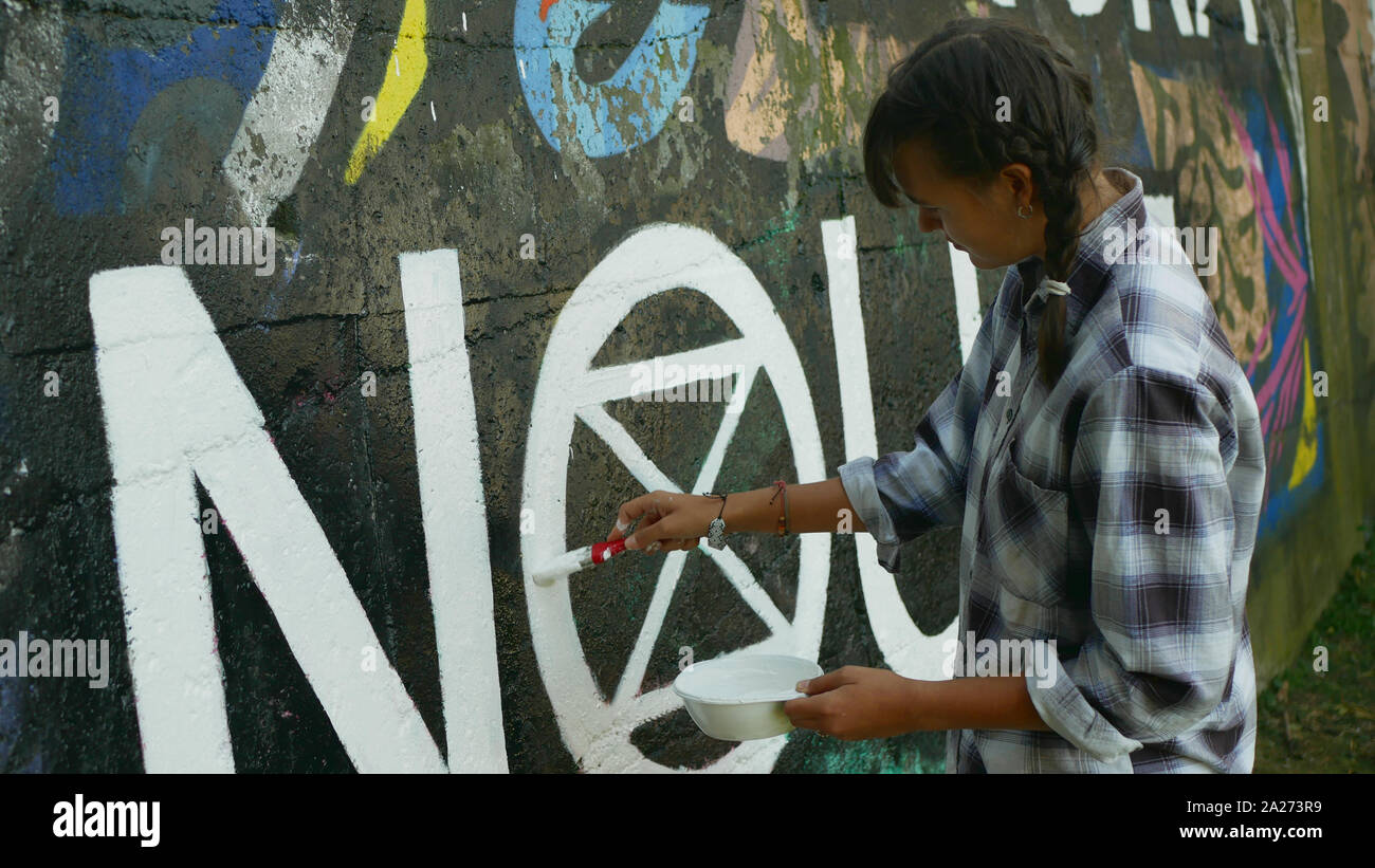 Mujer activista pinturas y repintado extinción símbolo de rebelión en pared legal para graffiti, demostración de acción contra el cambio climático, la gente Foto de stock