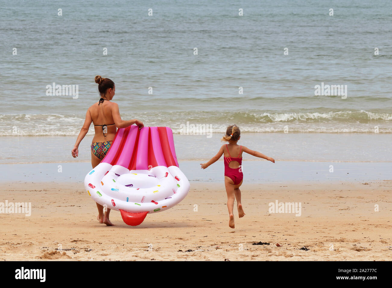 Madre e hija ir a nadar en el mar con colchón inflable. Chico alegre niña salta sobre la arena de la playa, vacaciones en la playa, infancia feliz Foto de stock