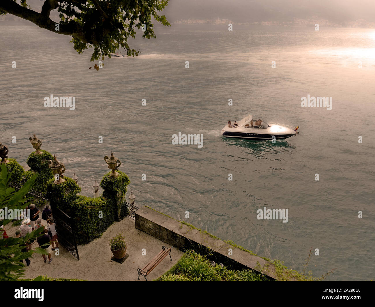 El Lago de Como, en Lombardía, Italia. Los turistas esperan su transporte de ferry mientras una lancha sppeds por Villa del Balbianello, cerca de Lenno, LAGO DE COMO Foto de stock