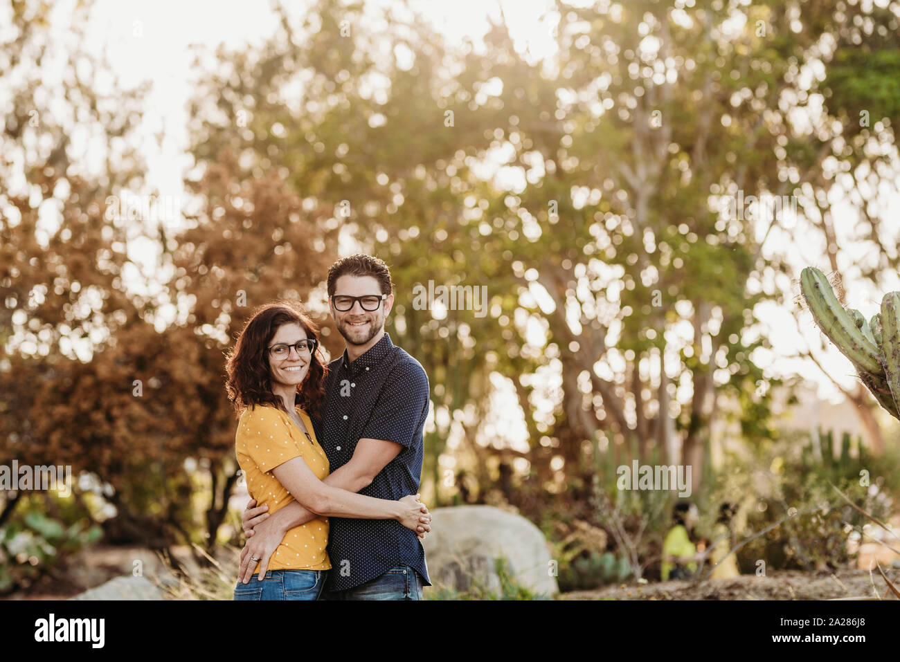 Retrato de marido y mujer sonriendo a la cámara en el soleado jardín de cactus Foto de stock
