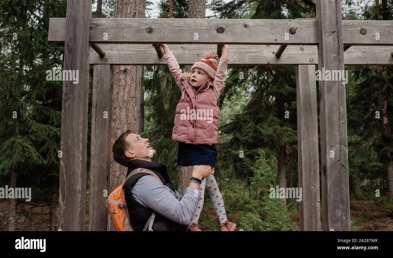 Papá ayudando a hija con barras de mono en un parque de ejercicio al aire libre Foto de stock