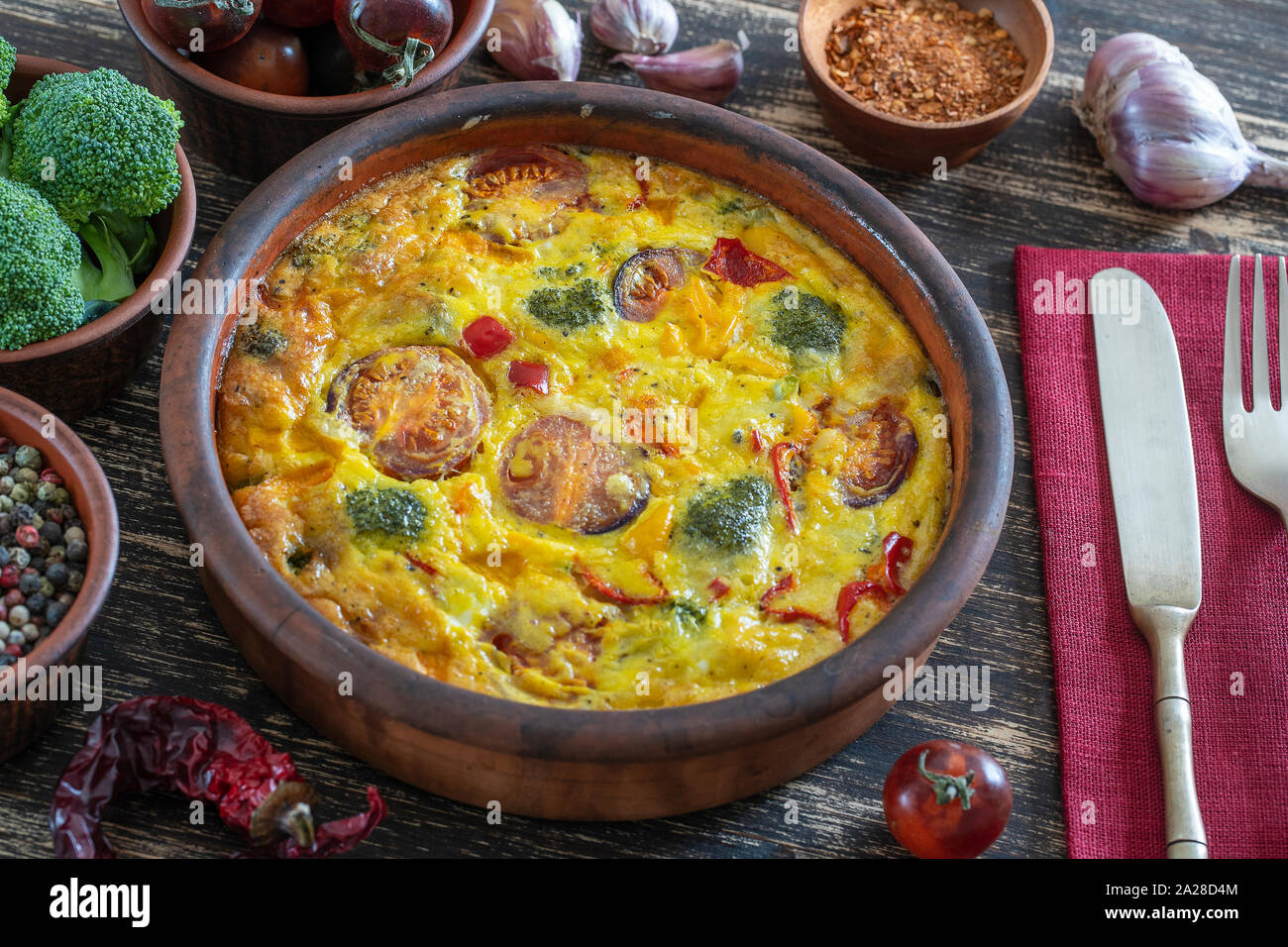 Cuenco de cerámica con verdura frittata, sencilla comida vegetariana. Frittata con huevo, tomate, pimiento, cebolla, brócoli y queso en la mesa de madera, de cerca. Foto de stock