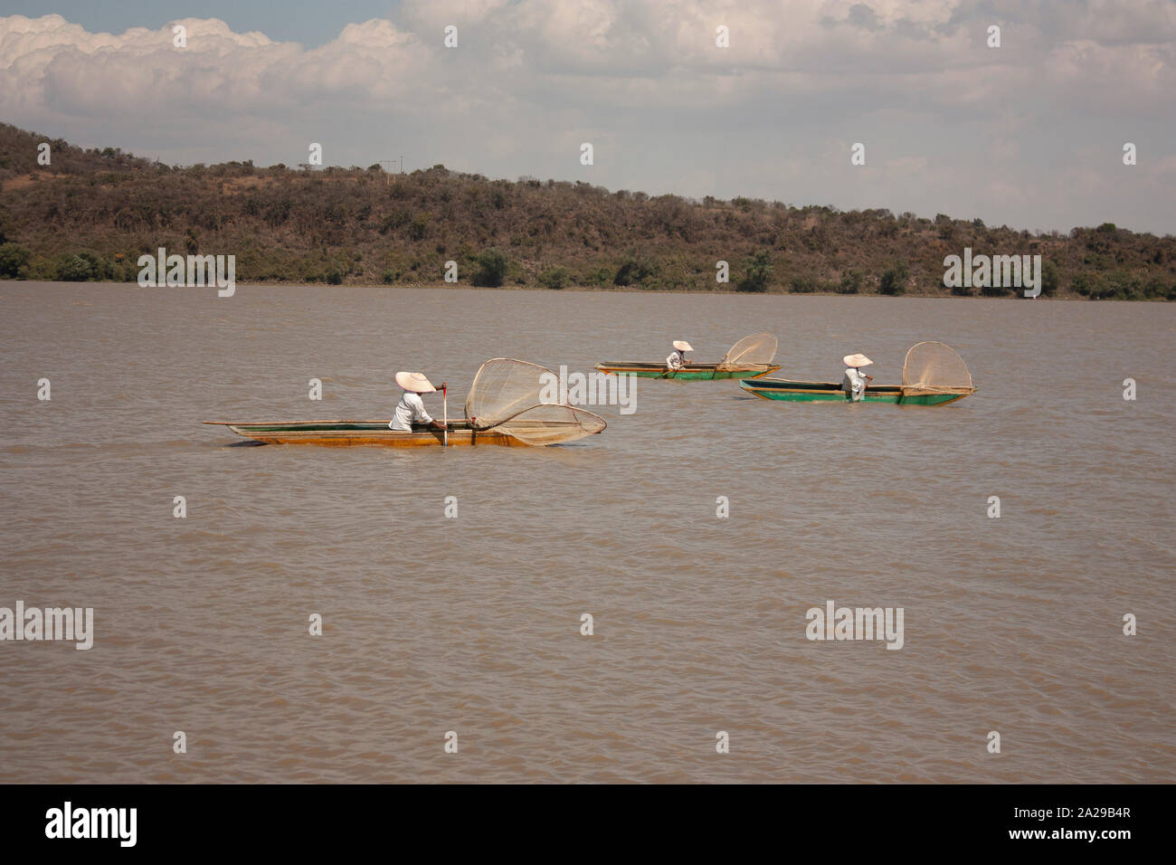 Trío de pescador, vistiendo ropa de manta y un sombrero blanco remando a  navegar con canoas cargadas con red de pesca al lago en México Fotografía  de stock - Alamy