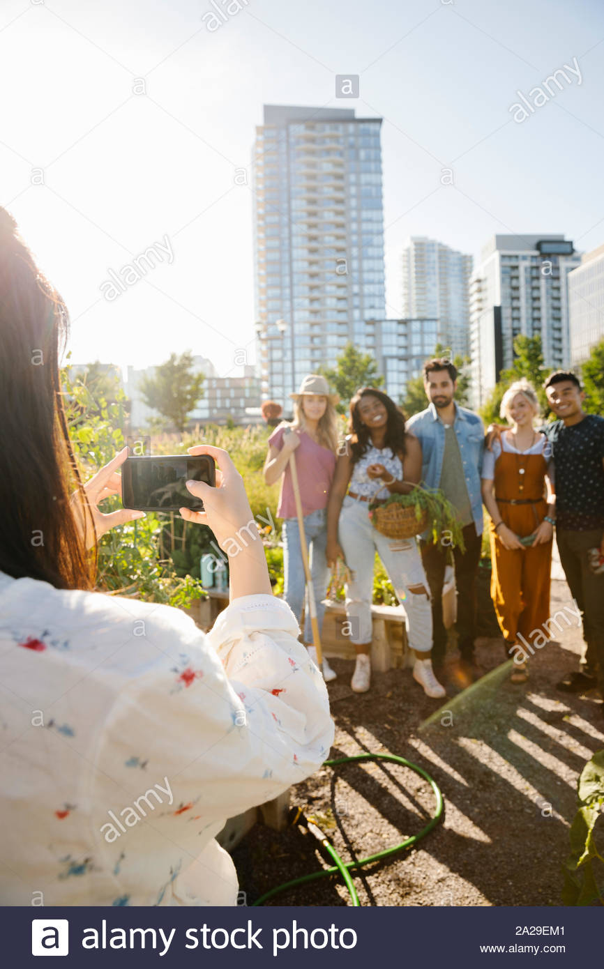 Mujer joven con cámara teléfono fotografiar amigos, comunidad urbana en el soleado jardín Foto de stock