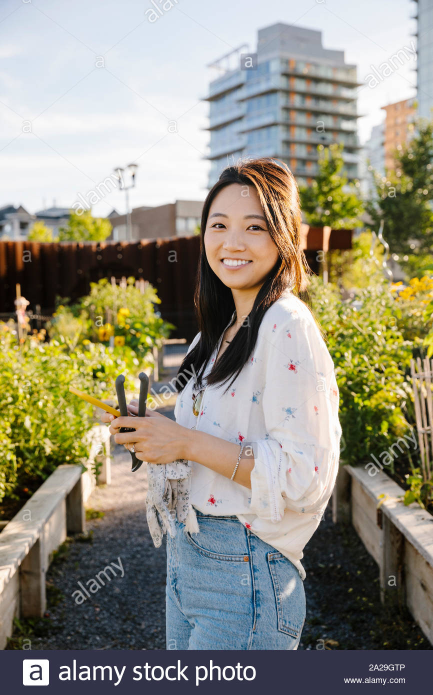 Retrato de mujer joven feliz con el teléfono inteligente en la soleada, jardín comunitario urbano Foto de stock