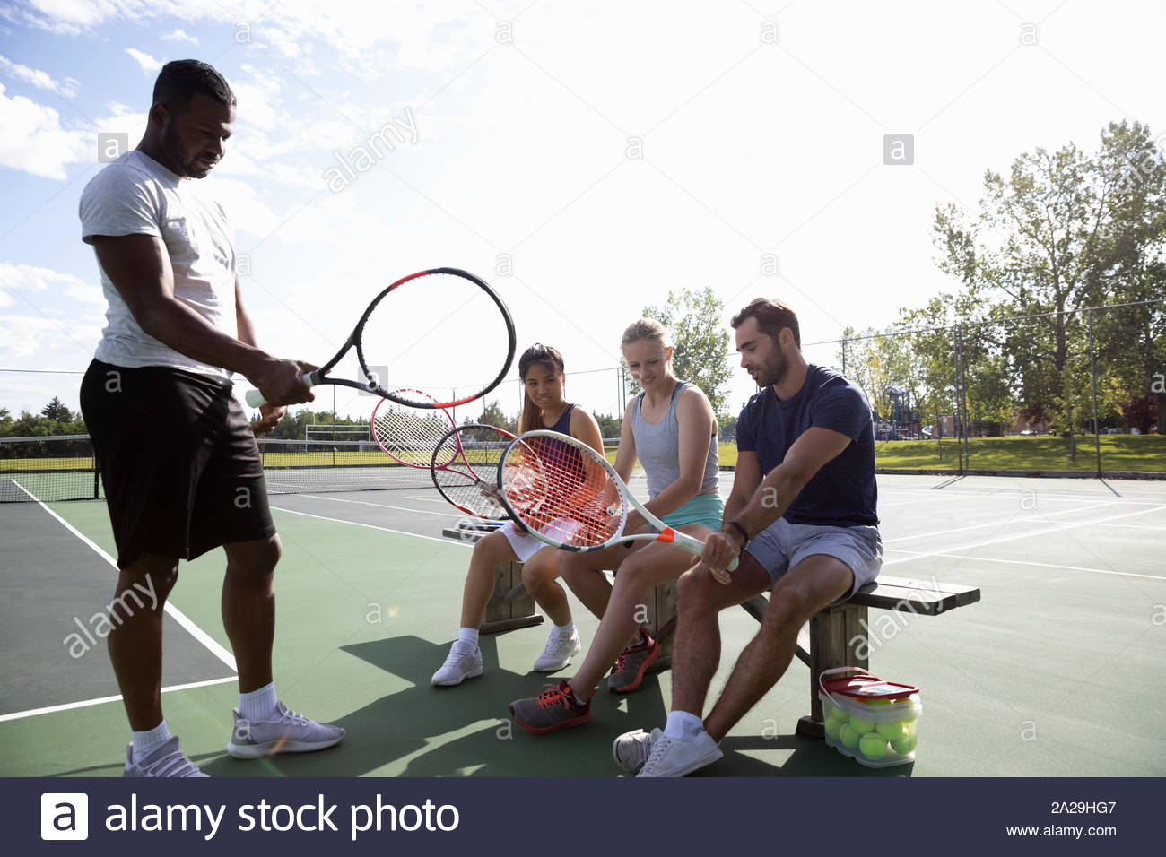 Joven amigos enseñando cómo para agarrar la raqueta de tenis en la cancha de tenis soleada Foto de stock
