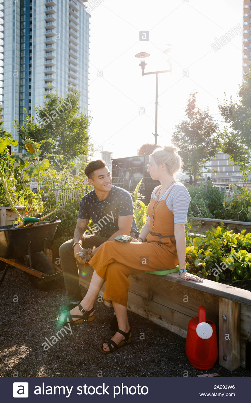 Pareja joven hablando en la soleada, jardín comunitario urbano Foto de stock