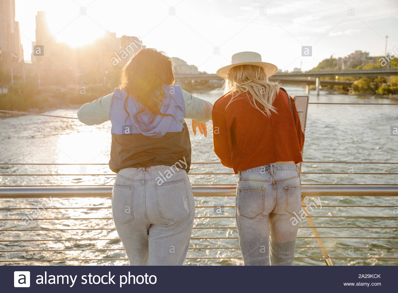 Las mujeres jóvenes amigos mirando río desde sunny, puente urbano Foto de stock
