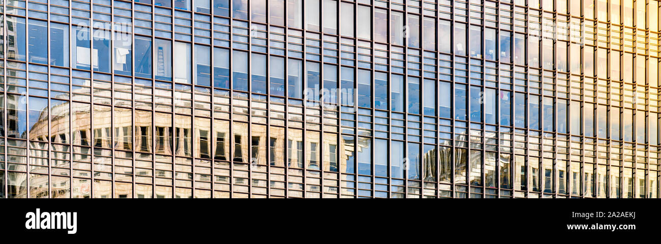 Panorámica de un edificio moderno de vidrio al atardecer con las nubes reflejándose en las ventanas de vidrio Foto de stock