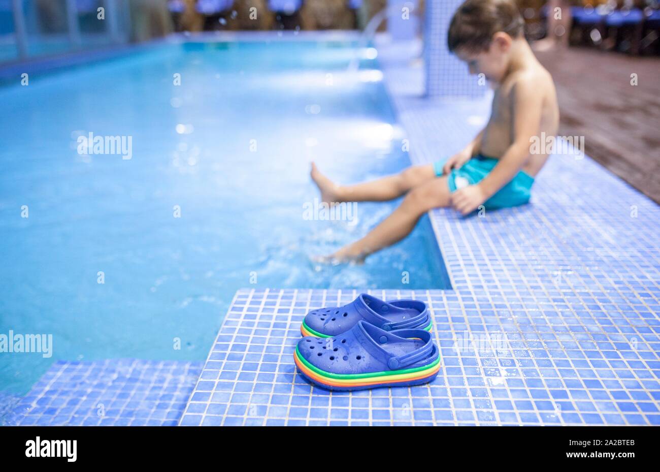 Niño de 4 años que salpica a piscina spa interior. Espuma taponan los zapatos en la vanguardia. Foto de stock