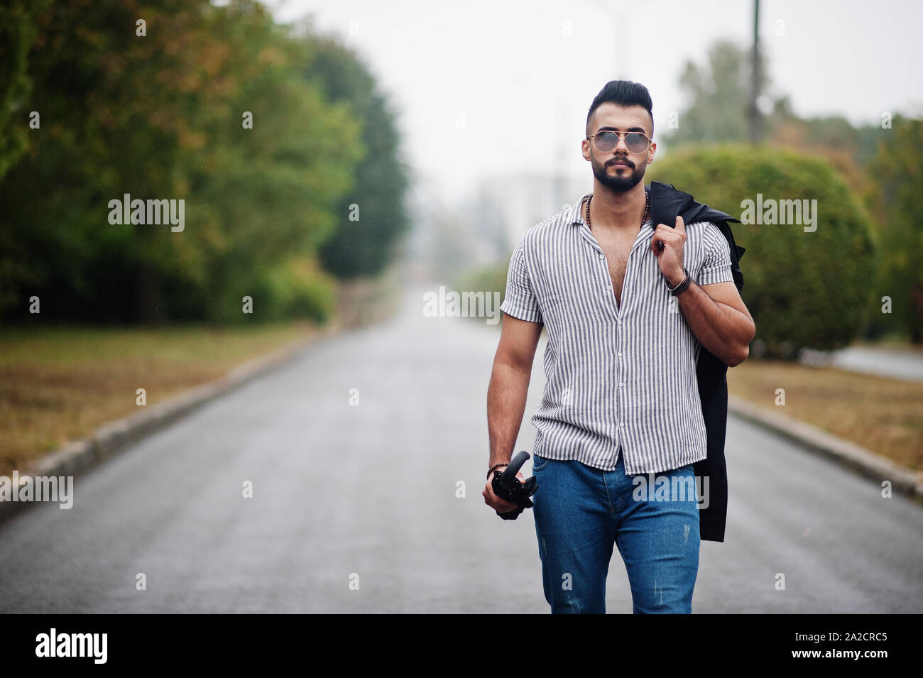Moda Hombre barba árabe alto desgaste en camisa, pantalones vaqueros y  gafas de sol caminando al parque con sombrilla y de abrigo Fotografía de  stock - Alamy