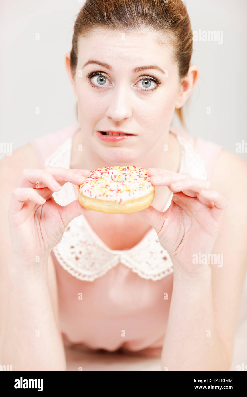 Mujer joven decida si va a comer un donut malsana expresando su culpabilidad. Foto de stock