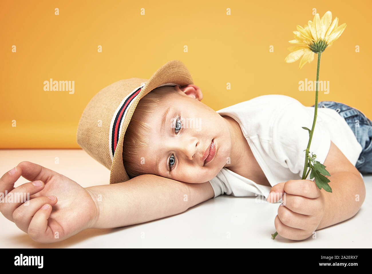 Retrato de un confidente poco feliz kid , posando en el sombrero de verano, la celebración de flor amarilla en la mano. Las emociones humanas, el concepto de expresión. Foto de stock