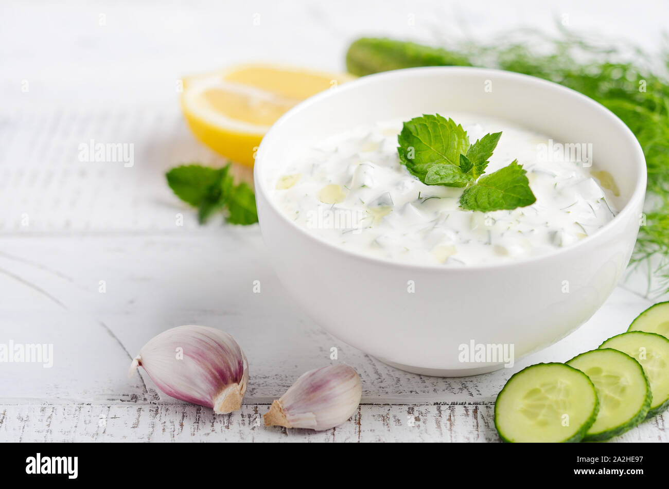 Salsa dip griego o vendaje tzatziki decorado con aceite de oliva y menta sobre mesa de madera blanca Foto de stock