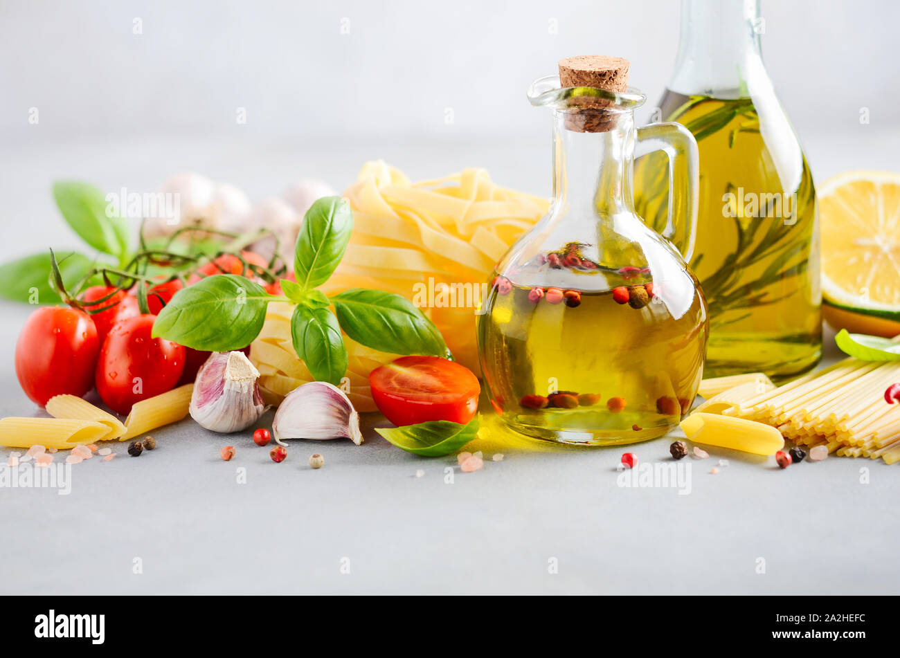 Ingredientes de comida italiana - pasta, tomate, albahaca y aceite de oliva sobre hormigón gris de fondo. Foto de stock