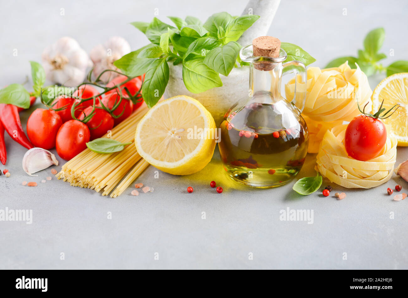 Ingredientes de comida italiana - pasta, tomate, albahaca y aceite de oliva sobre hormigón gris de fondo. Foto de stock