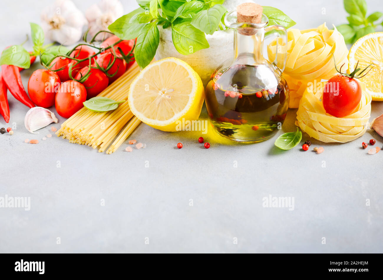 Ingredientes de comida italiana - pasta, tomate, albahaca y aceite de oliva sobre hormigón gris de fondo. Foto de stock