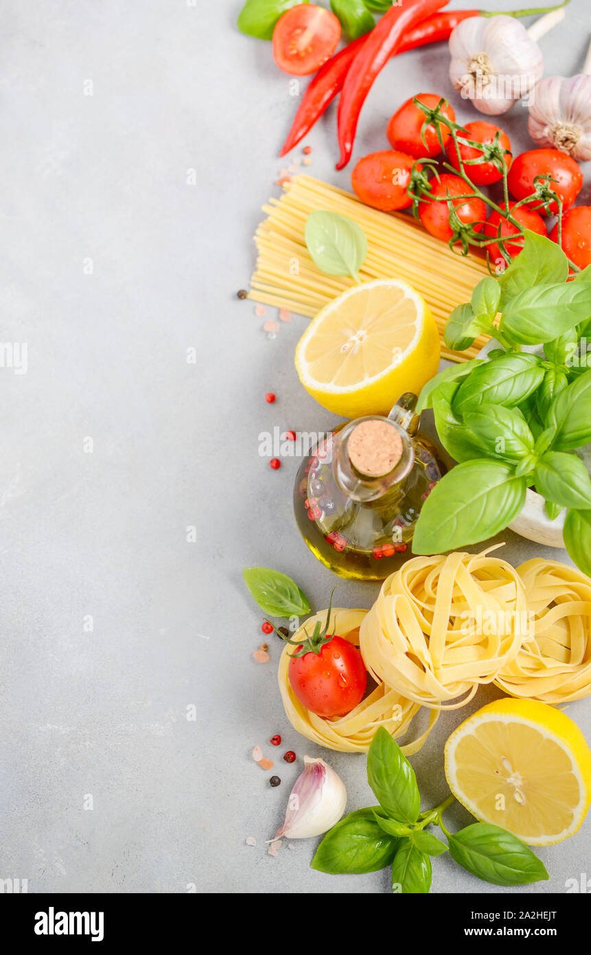 Ingredientes de comida italiana - pasta, tomate, albahaca y aceite de oliva sobre hormigón gris de fondo. Foto de stock