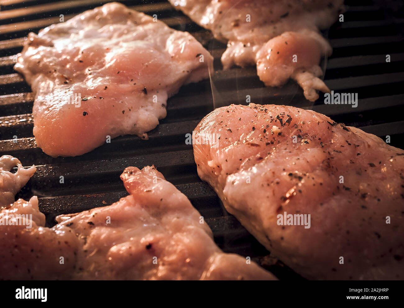 Fumante asar pollo o pavo crudo filetes de carne condimentada con especias en parrilla eléctrica placa. Foto de stock