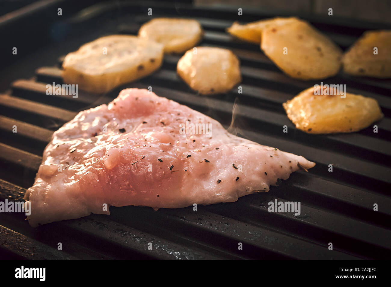 Asar pollo crudo fumante o filete de carne de pavo y patatas condimentadas con especias en parrilla eléctrica placa. Foto de stock