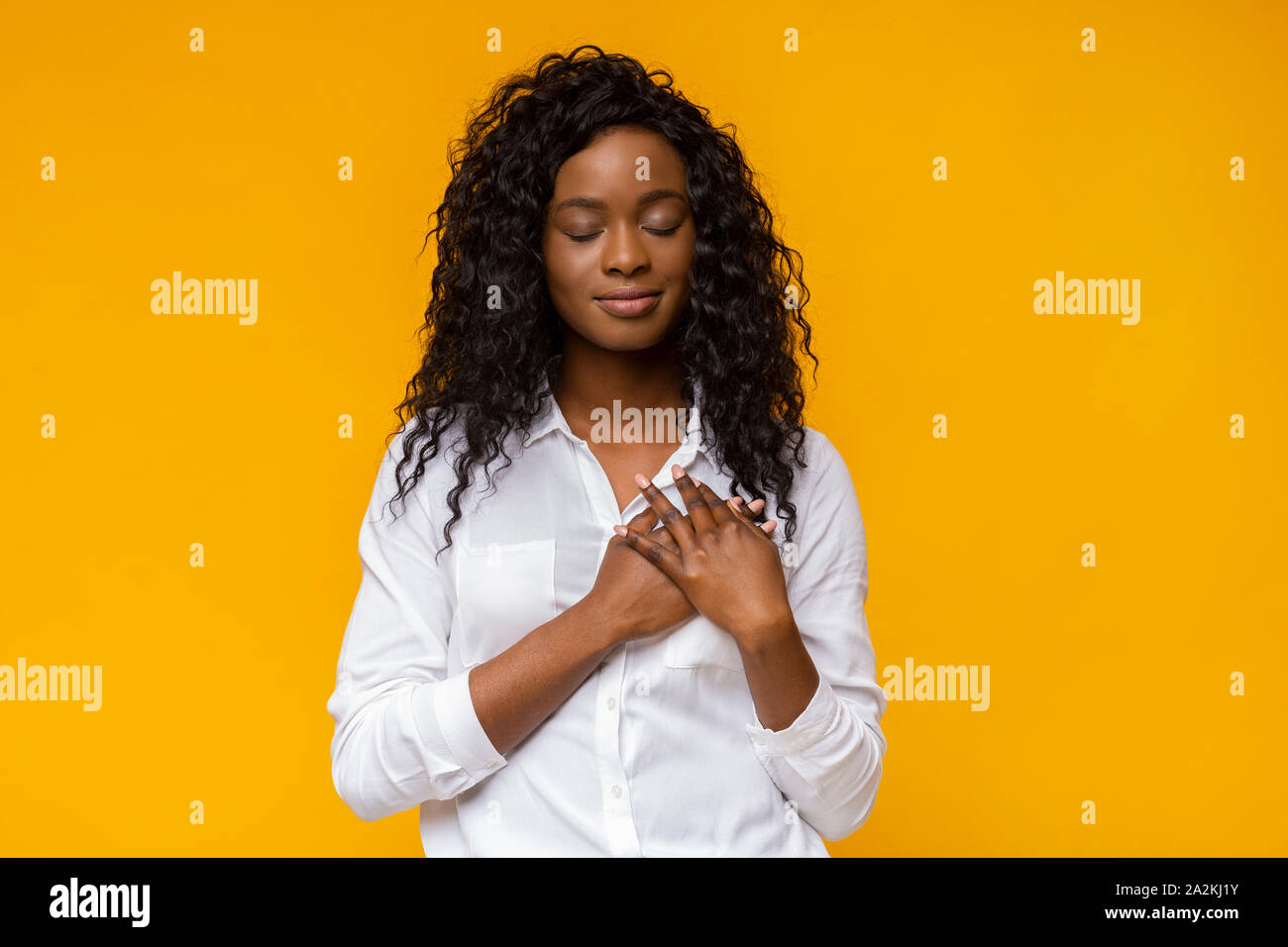 Agradecida mujer afro colocando las manos sobre su corazón Foto de stock
