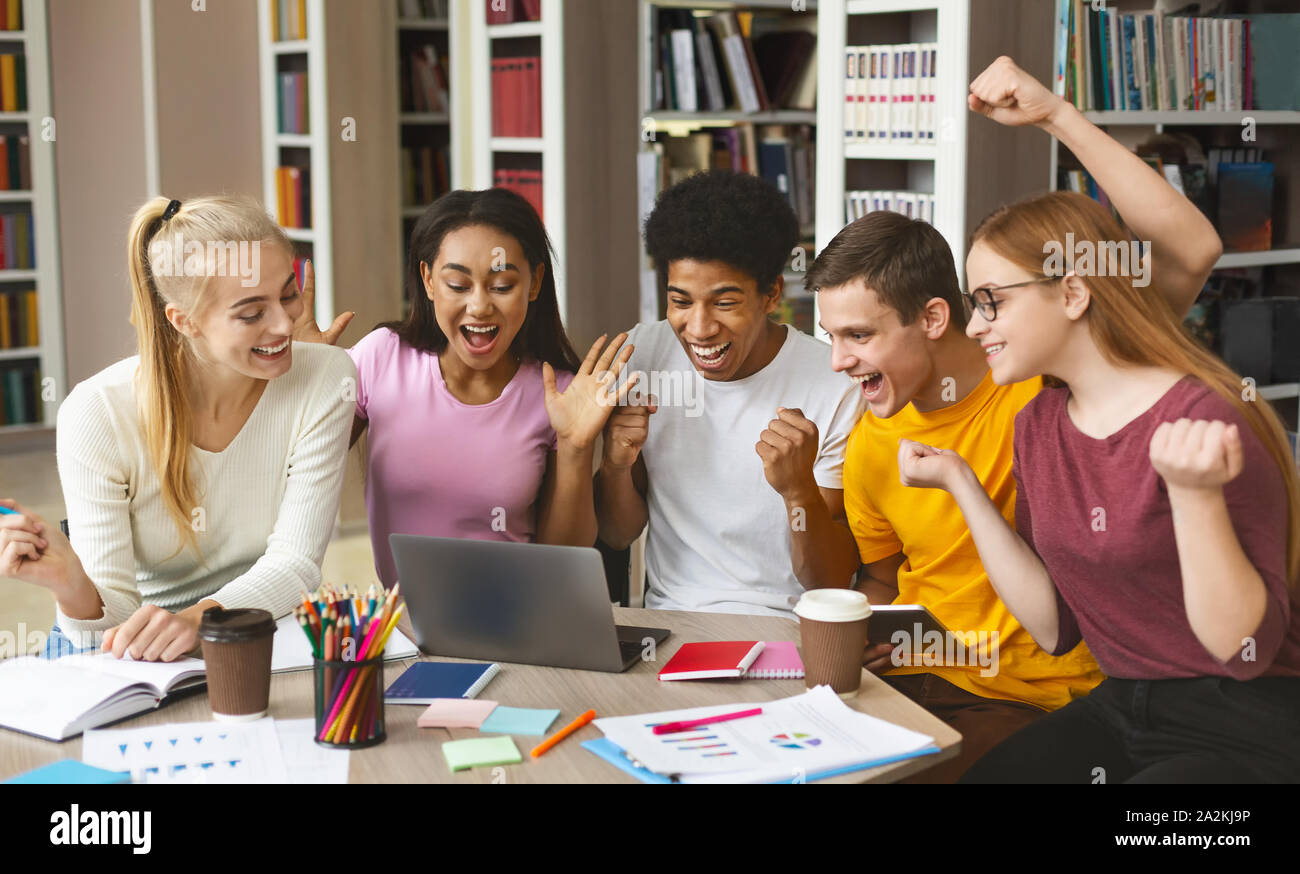 Grupo de jóvenes estudiantes felices disfrutando de los resultados de la prueba en la biblioteca Foto de stock
