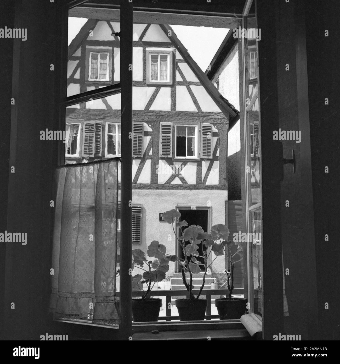 Blick durch ein auf ein Fachwerkhaus geöffnetes Fenster, Deutschland 1930er Jahre. Ver a través de una ventana abierta en una casa de madera, Alemania 1930. Foto de stock