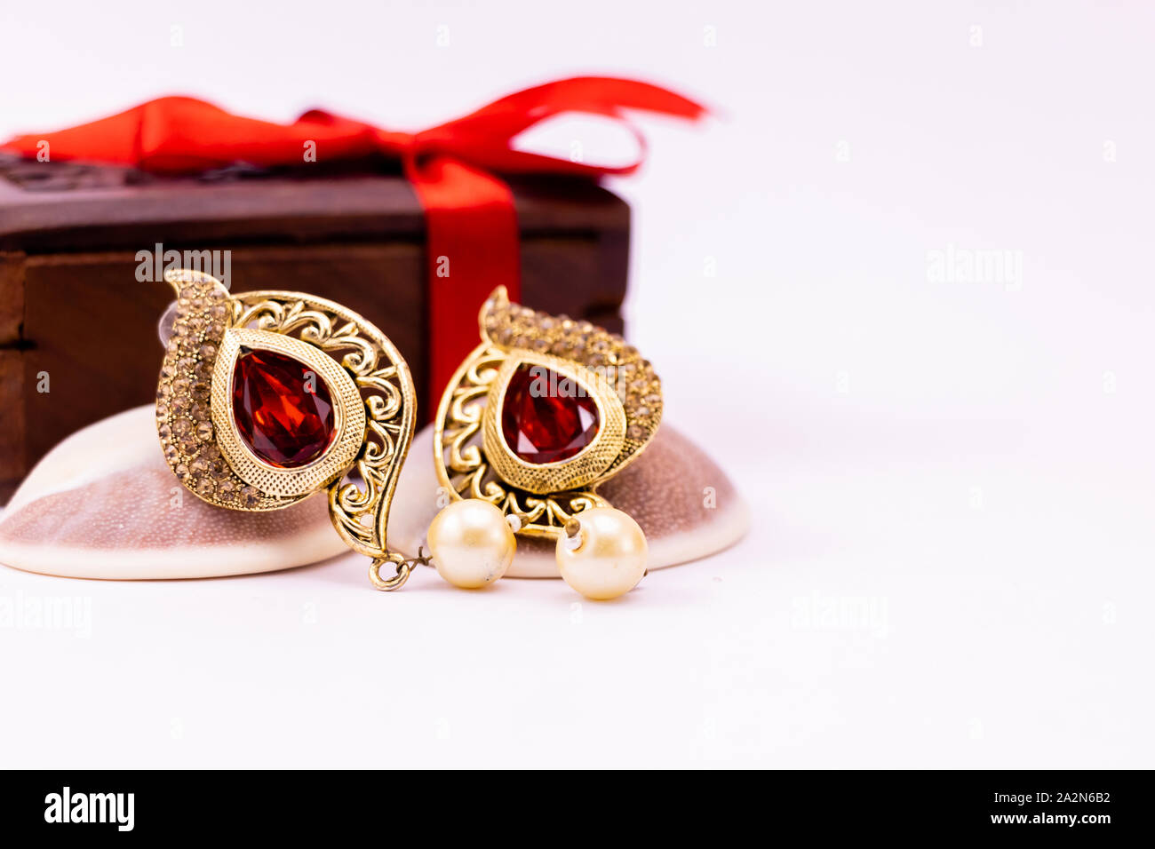 Golden earring de conchas y caja de regalo de madera decorada con una cinta roja sobre fondo blanco. Concepto de regalo de aniversario Foto de stock