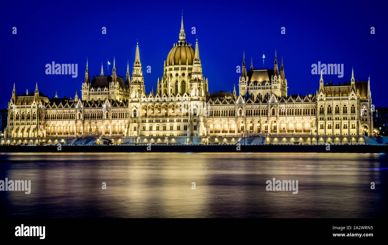 El Parlamento Húngaro iluminado por la noche con la luz amarilla y la reflexión del agua. Budapest, Hungría. Foto de stock