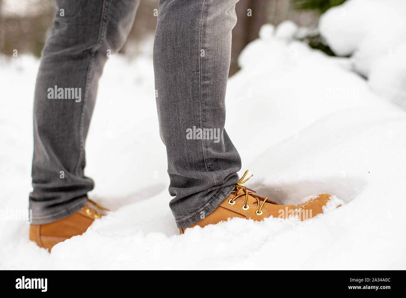 Las piernas de un hombre en amarillo moda zapatos están de pie en un  ventisquero, contra un fondo borroso de un bosque cubierto de nieve en  invierno. Close-up Fotografía de stock -