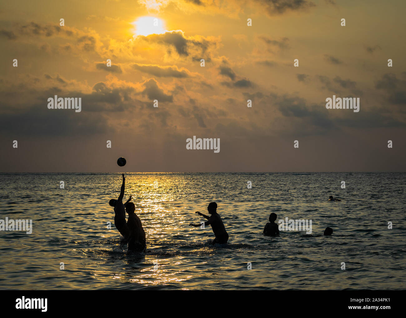 Siluetas de grupo de boy están jugando una bola en el mar al atardecer. Foto de stock